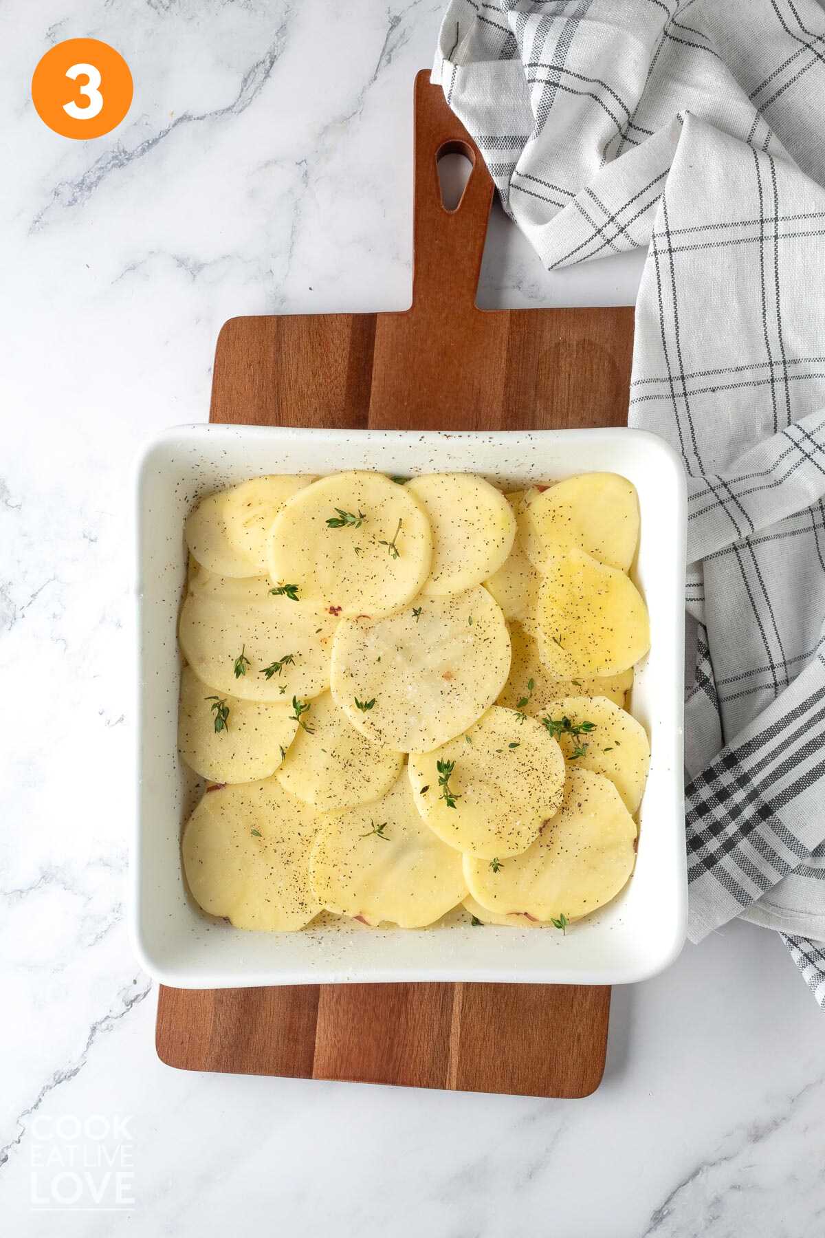 Potatoes layered in a baking dish and sprinkled with salt and pepper.