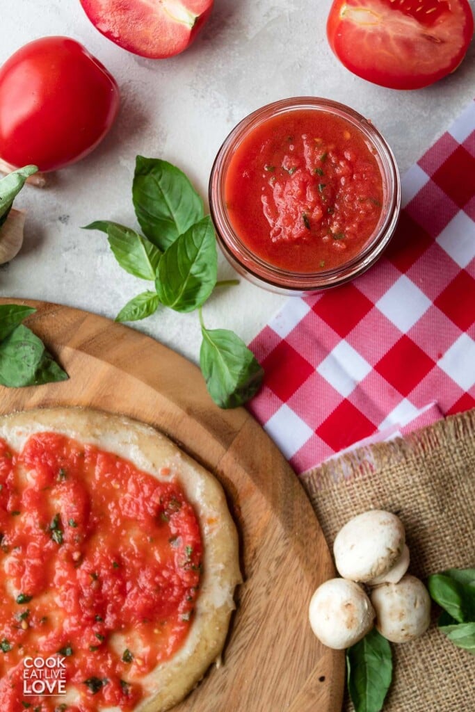 Authentic italian pizza sauce with fresh tomatoes spread on a crust and in a jar.
