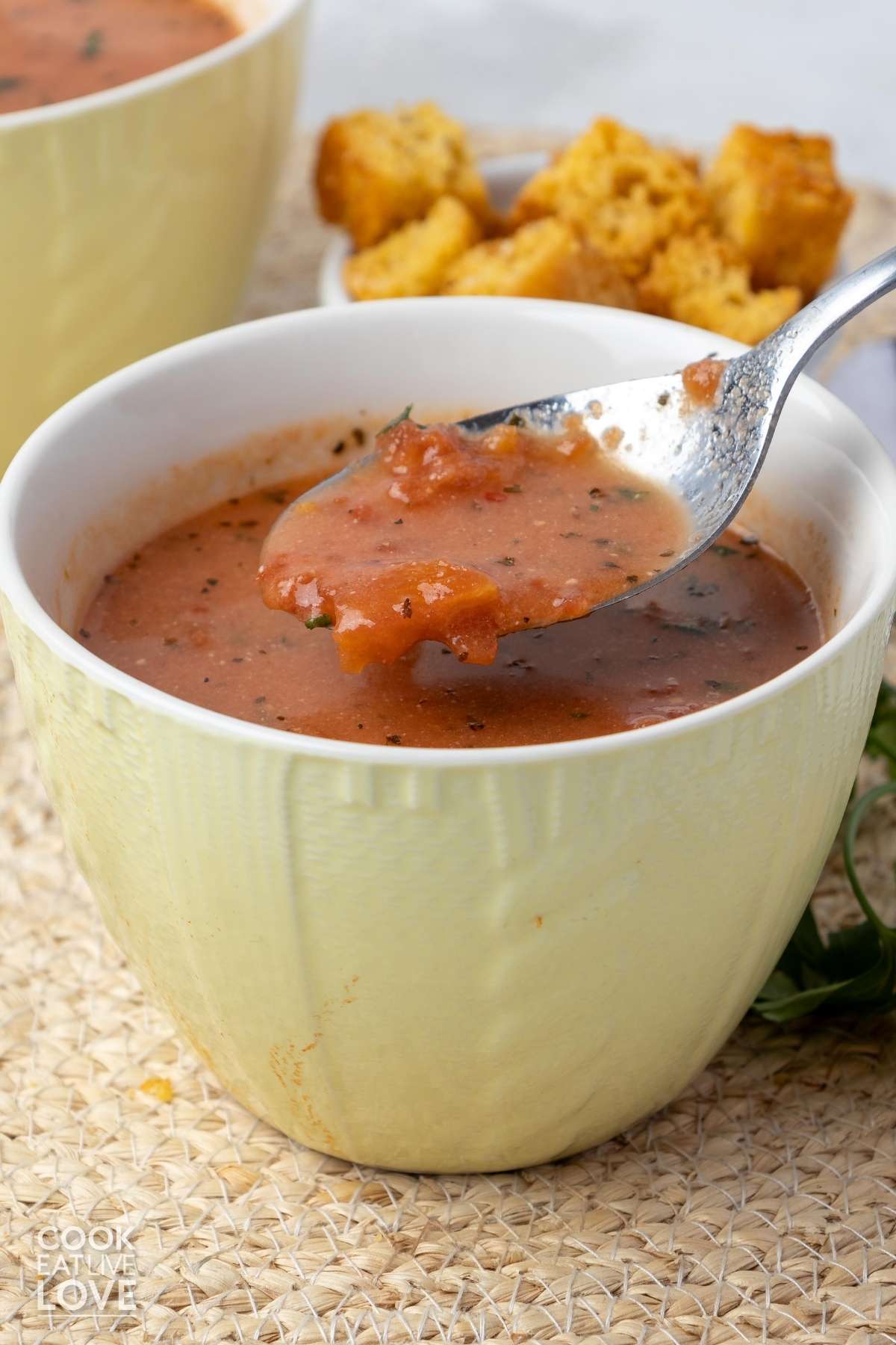 A spoon holding a spoonful of vegan tomato soup up over a cup of soup.