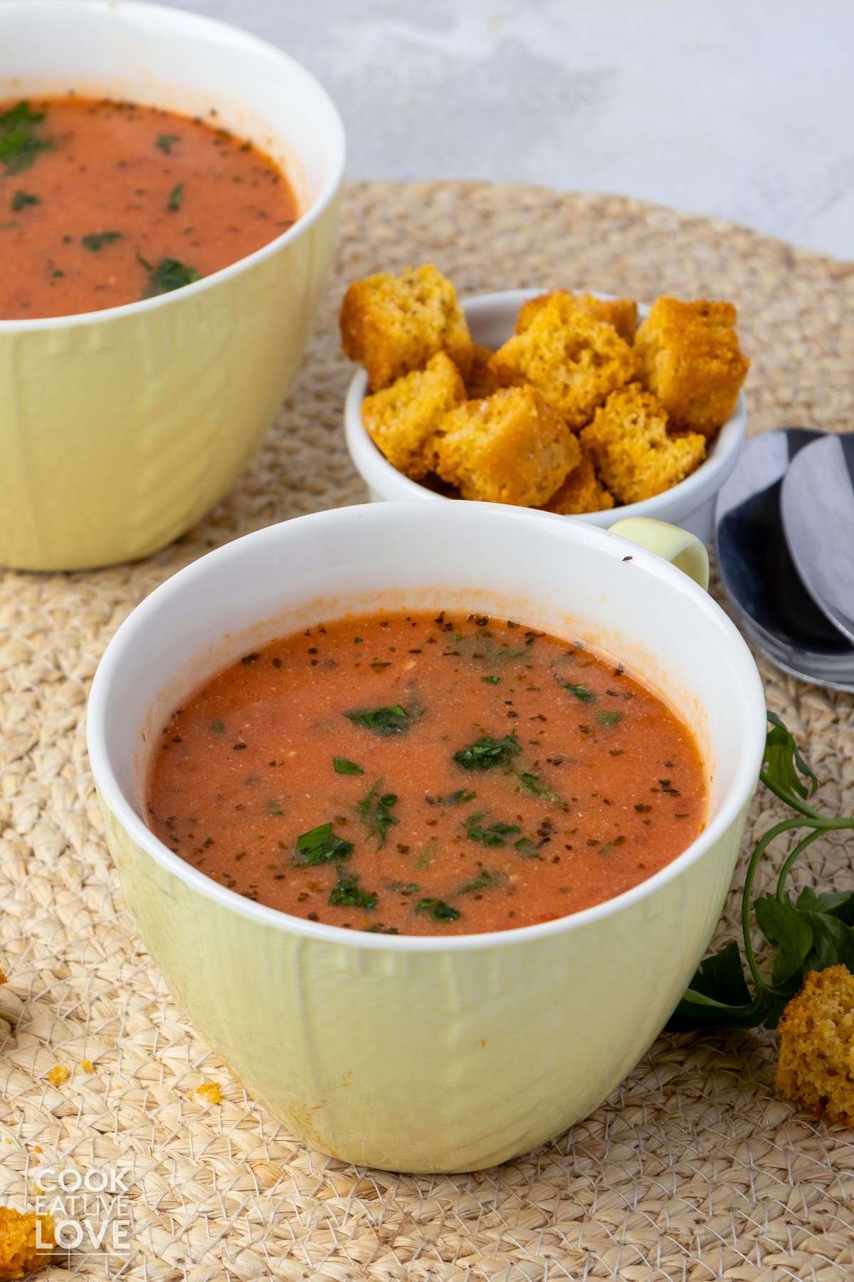 A bowl of dairy free tomato soup on the table with some croutons in the background with another cup.