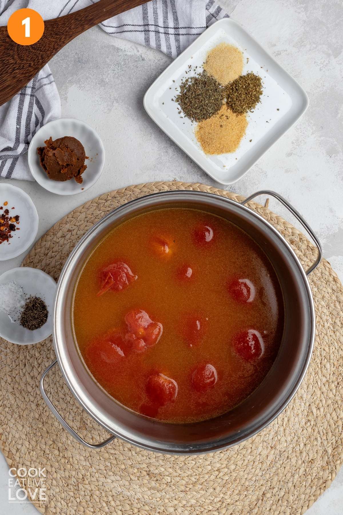 Canned tomatoes in a pot with the seasonings on a plate and little bowls on the side.