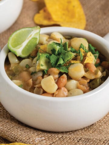 Overhead photo of bowl of white bean chili ready to eat. Shown with some topping ideas including avocado, cilantro and salsa.