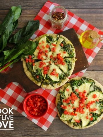 Two pesto and veggie pizzas on a table