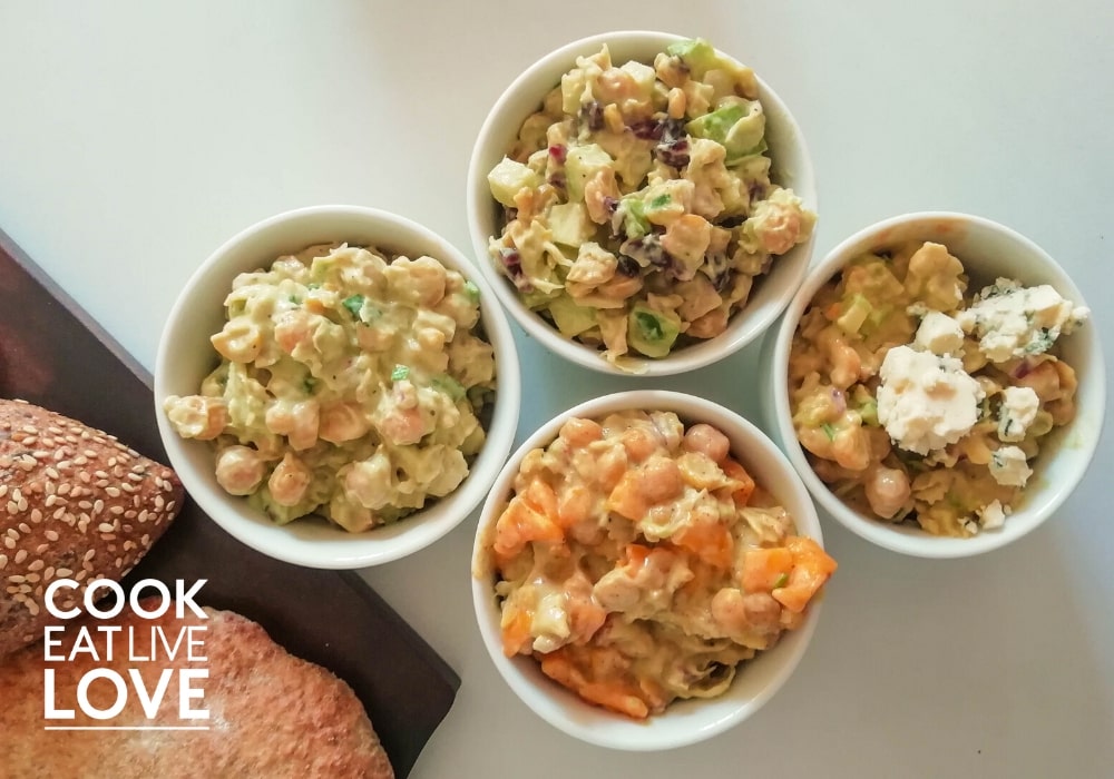 Four different flavors of creamy chickpea salad in white bowls on white background .