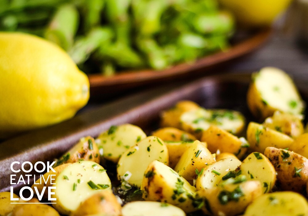 Lemon roasted potatoes on baking sheet with veggies and whole lemon in back .