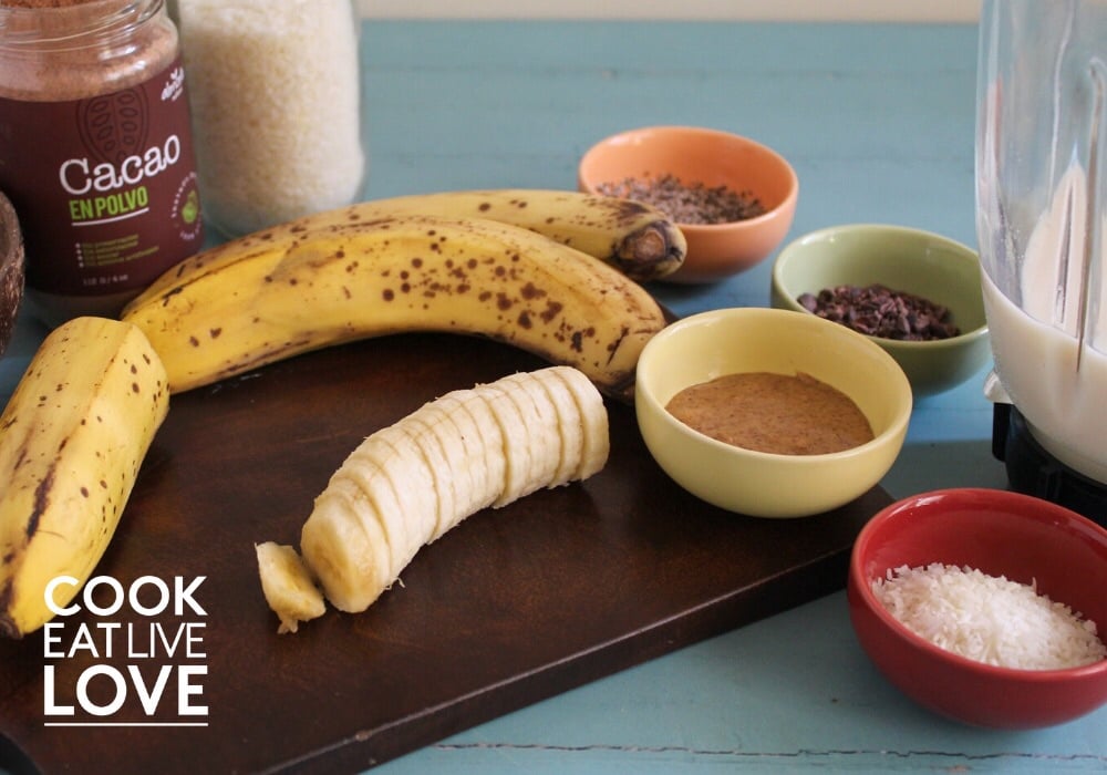 The ingredients for this smoothie bowl recipe are shown with cut banana on wood cutting board