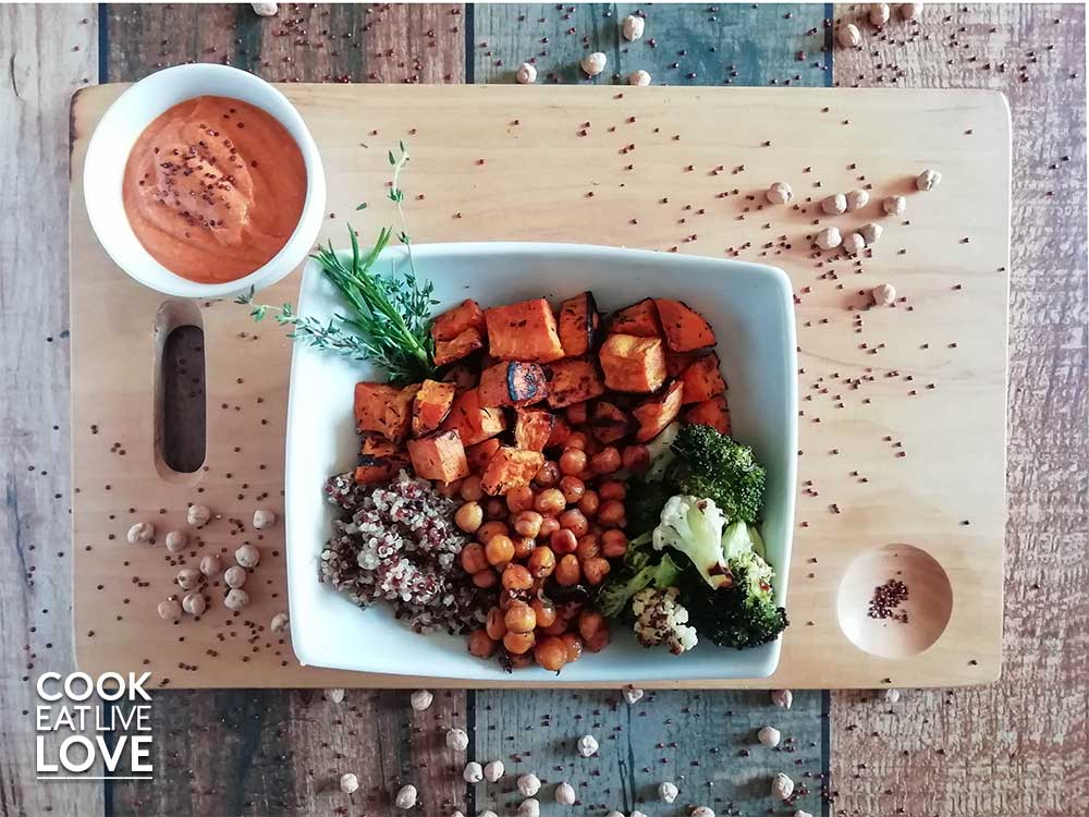 Bowl of roasted chickpeas , veggies and sweet potato in white square bowl on wooden cutting board .
