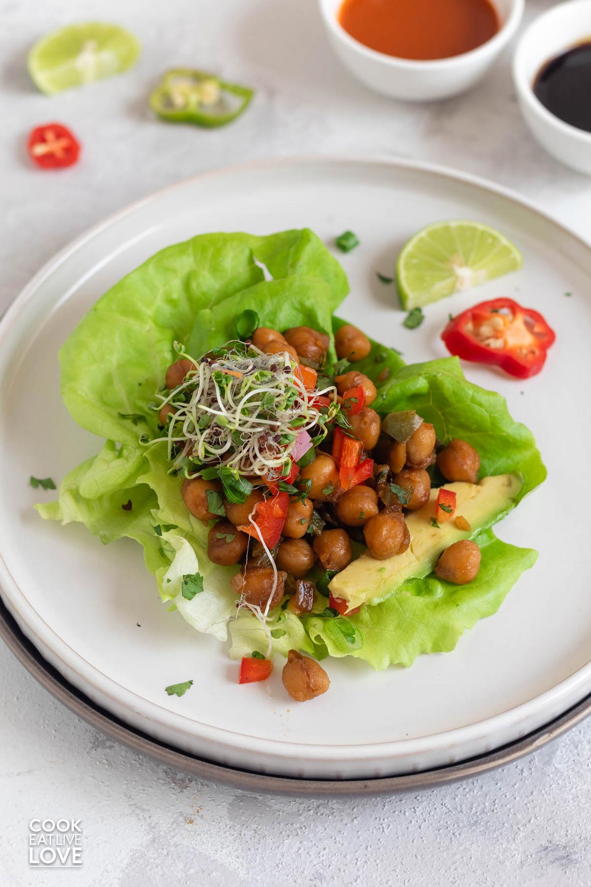 On a white rectangle two lettuce leafs are filled with buffalo chickpeas and ready to eat.