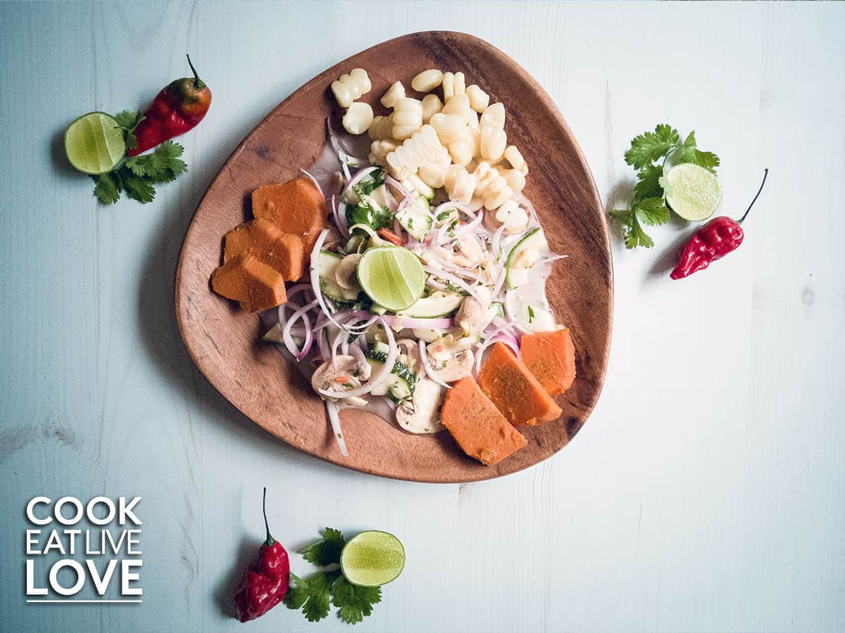 Vegetable ceviche is served up on wooden triangular plate with sweet potato and choclo.