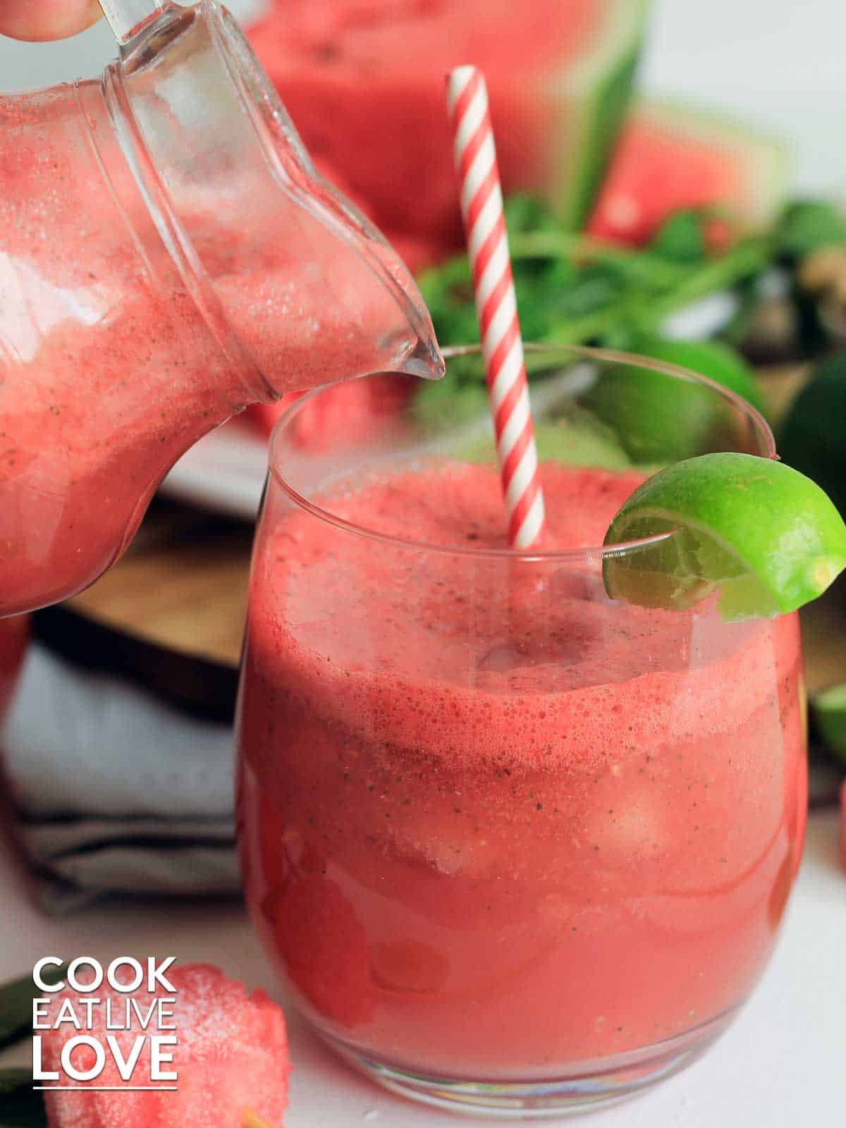 Frozen watermelon drink in a glass in front of a stack of watermelon slices and a pitcher of extra slushie.