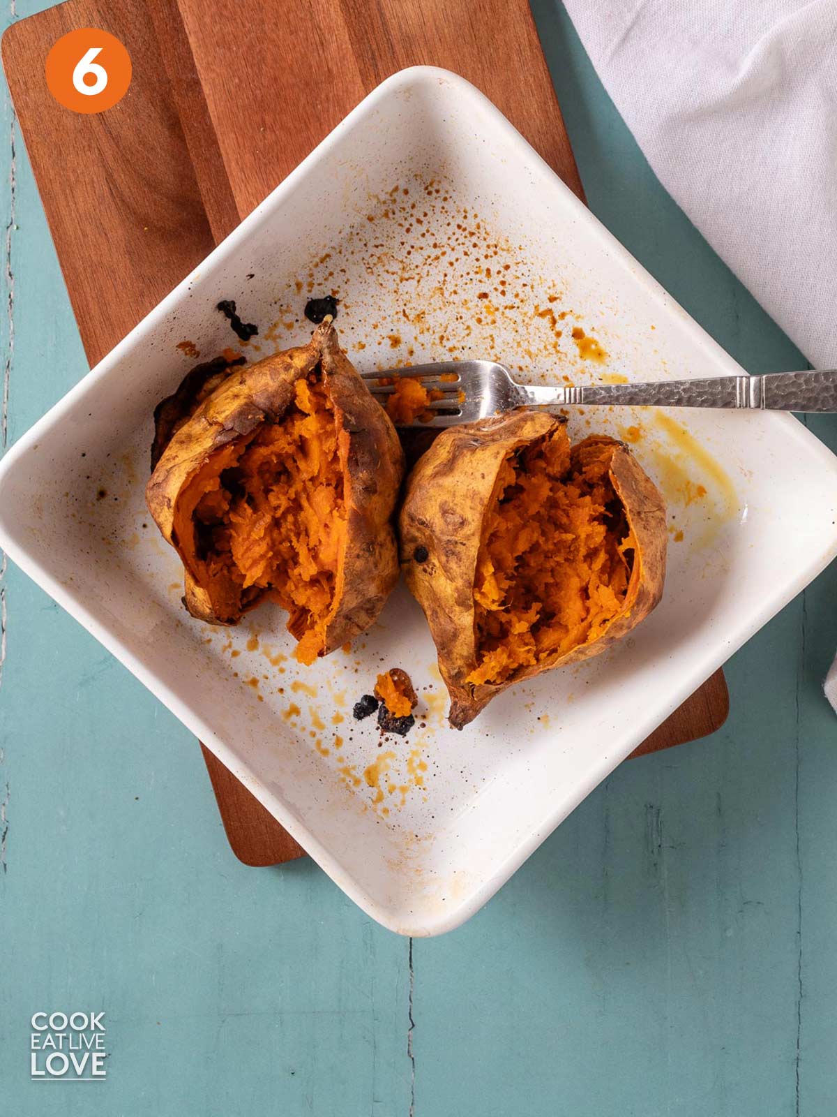 Two sweet potatoes in a baking dish cut open and mashed inside the jackets.