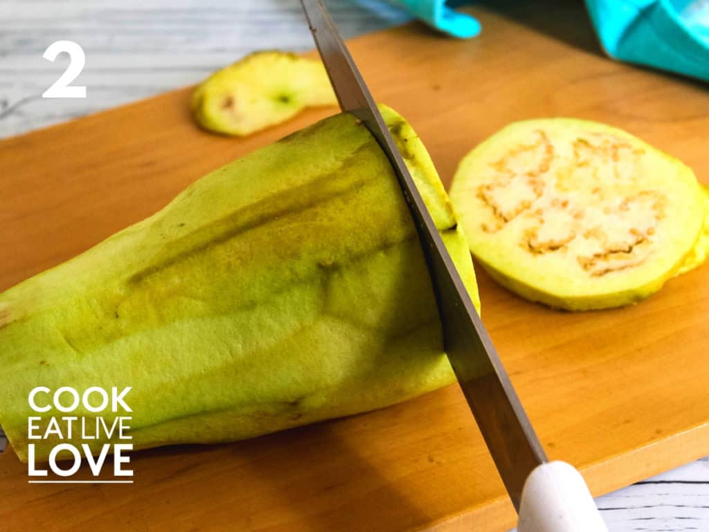 Peeled eggplant is on a cutting board and a knife is shown cutting it into slices.