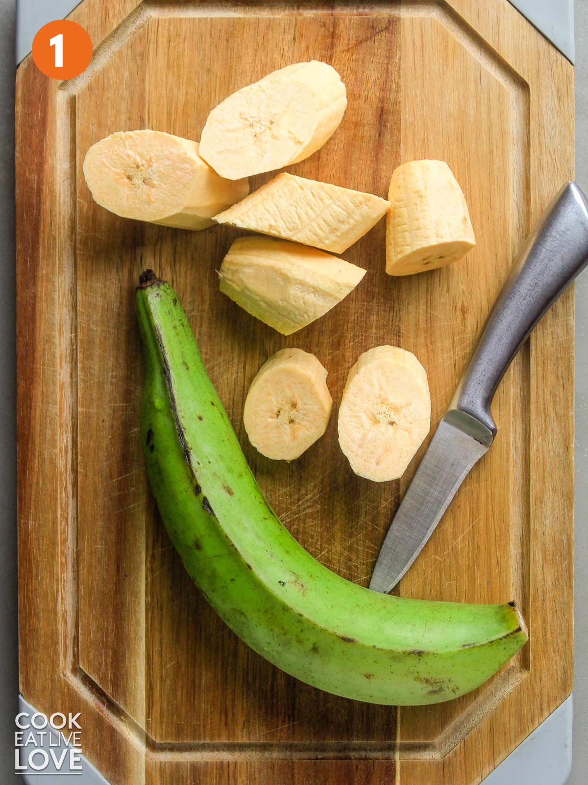 Plantains cut into one inch pieces on a cutting board with a knife and a whole plantain.