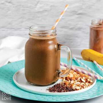 A large glass mug of chocolate smoothie on an aqua colored plate.