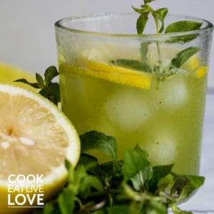 A closeup of glass of cucumber mint lemonade with some fresh mint and lemon half.