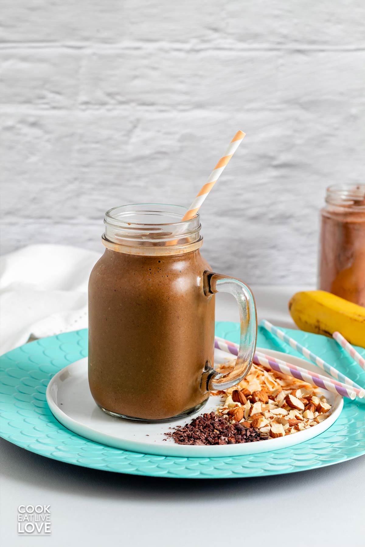 A chocolate smoothie in a large glass mug with a straw and toppings on a plate.