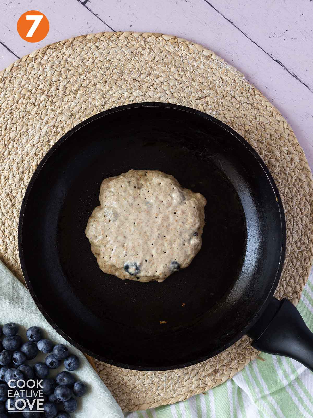Vegan blueberry chia pancakes cooking in a pan ready to flip.
