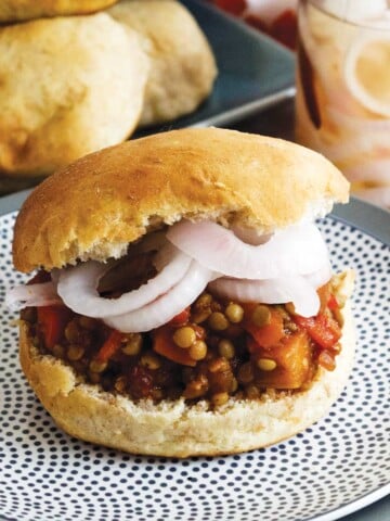 Sloppy joe on a plate with onions and buns behind