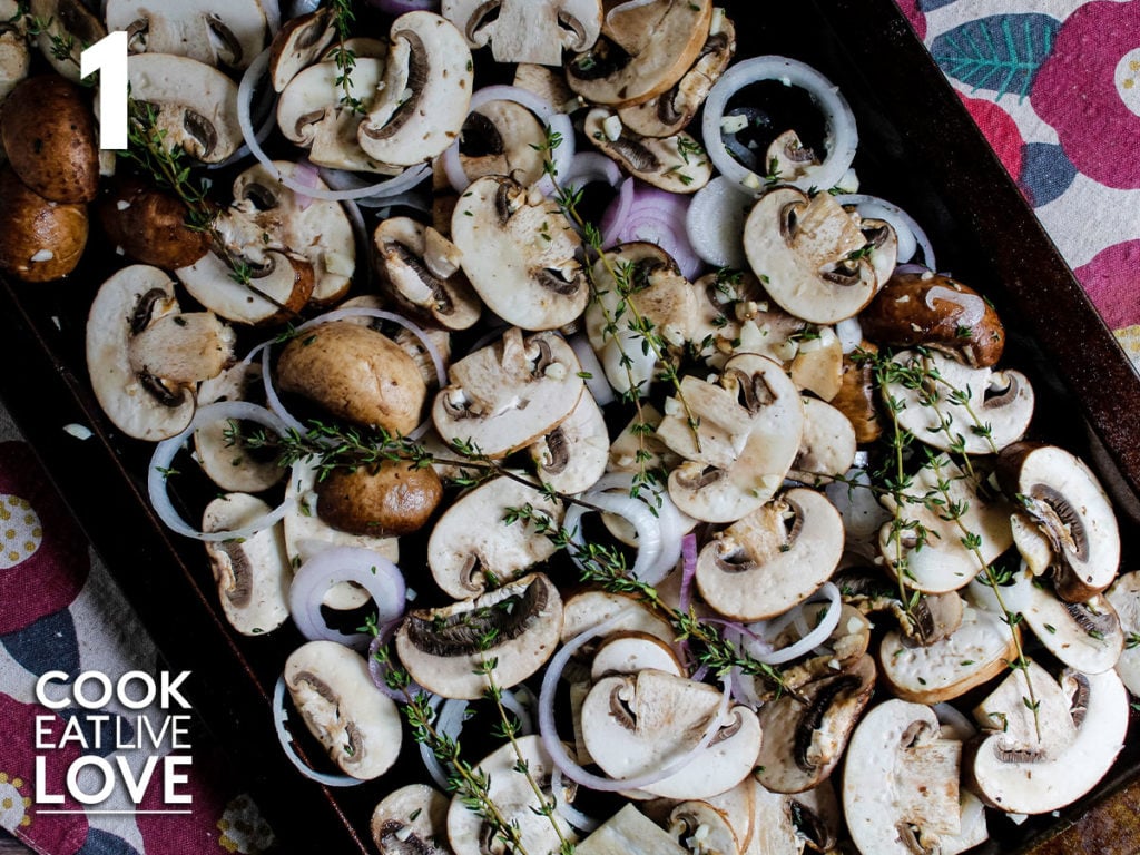 Uncooked mushrooms and onions are on a baking sheet topped with sprigs of fresh thyme.