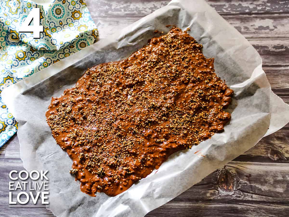 Quinoa chocolate is spread out on a baking sheet and topped with caramelized quinoa and sea salt.