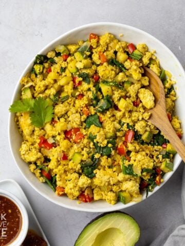 Tofu scramble with veggies in a bowl with a spoon resting in the dish.