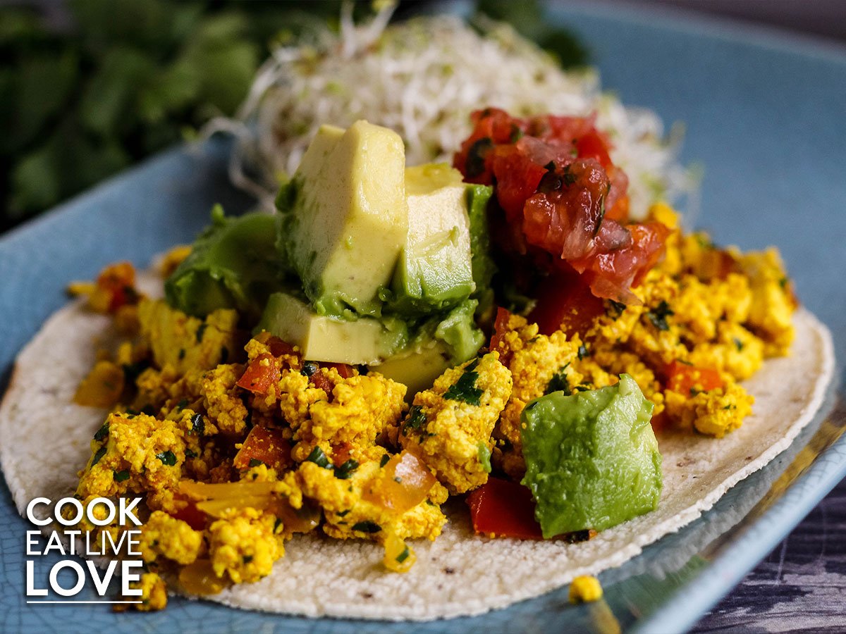 Closeup from the front of the tofu scramble tacos all ready to eat.  Yellow tofu that look like scrambled eggs, avocado and salsa.
