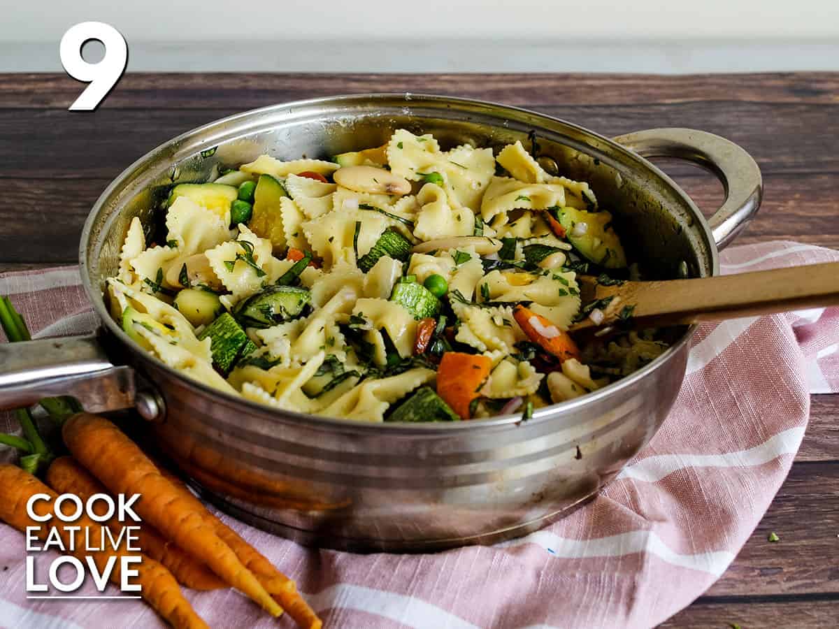 Pasta and vegetables mixed in skillet with wooden spoon.