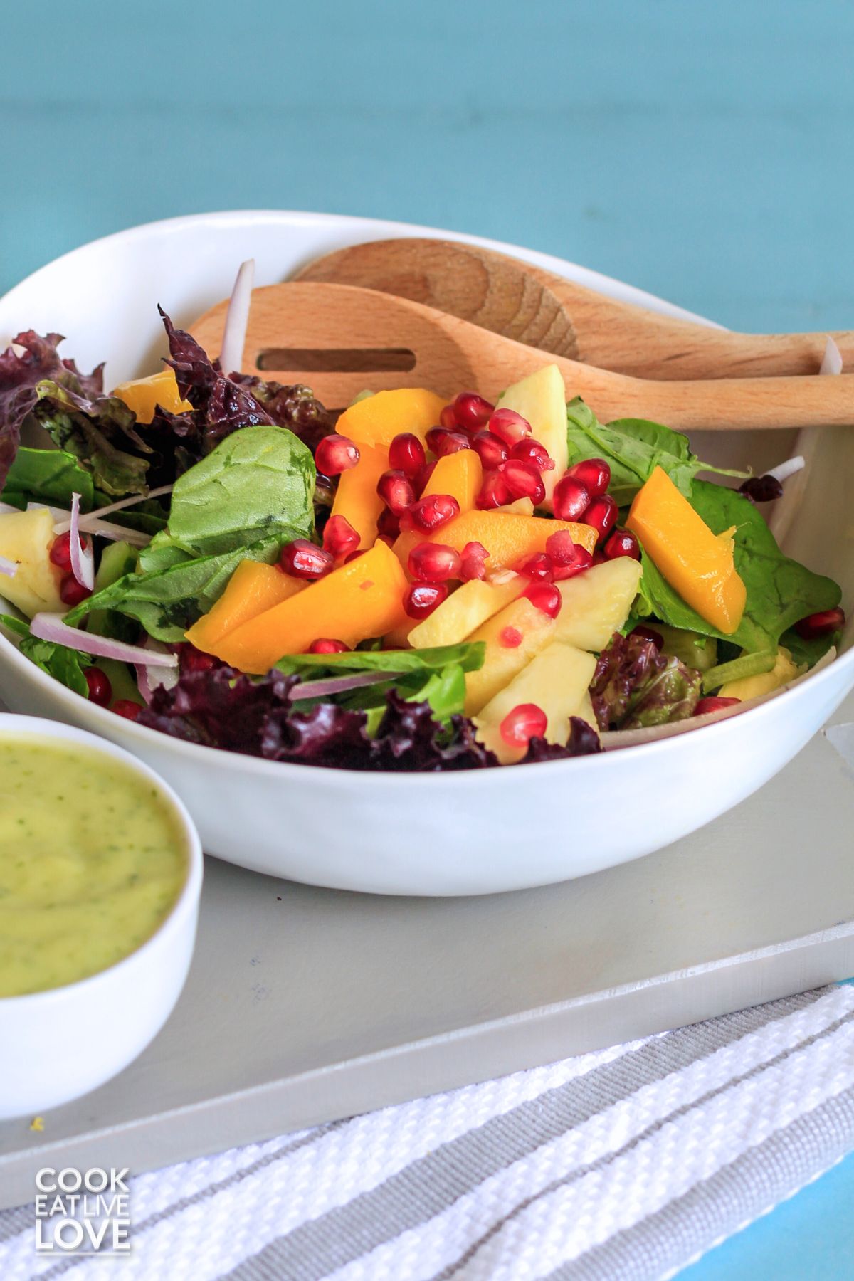 A bowl of tropical salad with mango and pineapple with wooden spoons resting in the back.