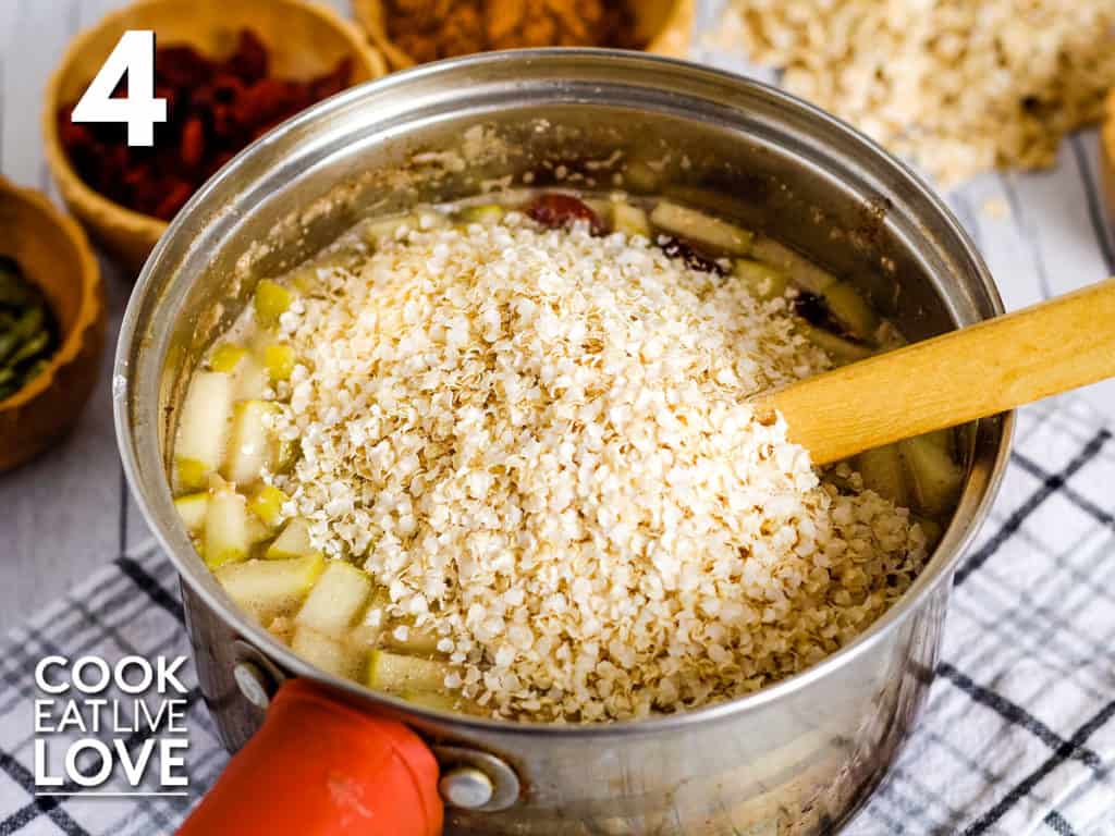 Overhead view of quinoa flakes added to the pot with a wooden spoon to the side. 