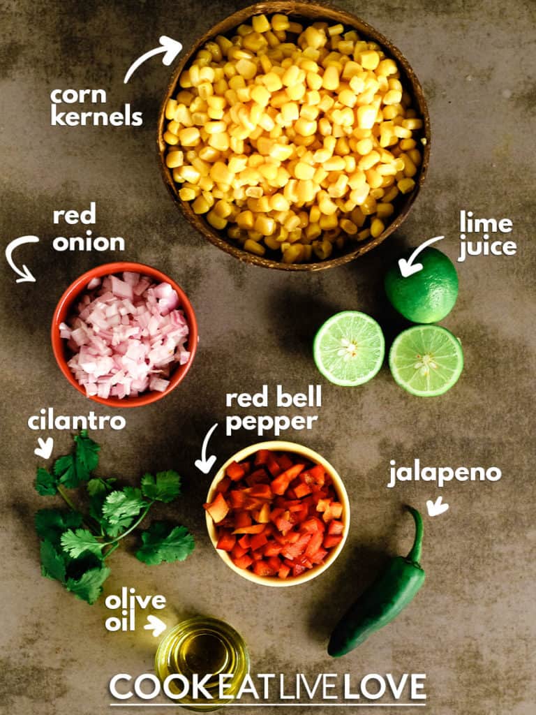 Overhead view of ingredients for roasted corn salsa:  corn kernels, limes, jalapeno, red bell pepper, olive oil, cilantro and red onion.