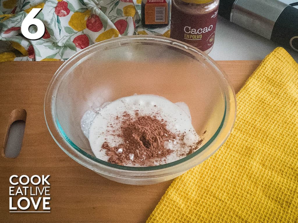 Cacao powder is added to the coconut cream in a glass bowl.