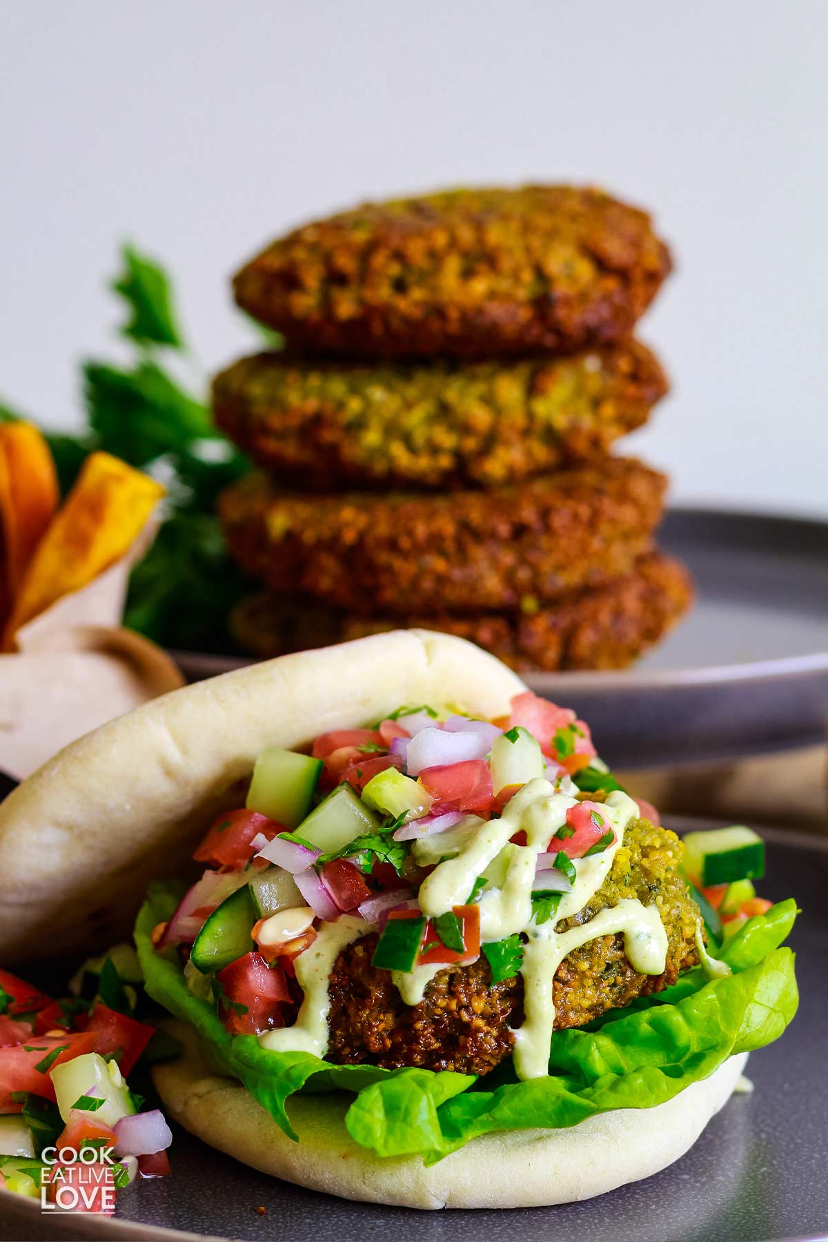 Front view of finished vegan falafel burger.  Stack of patties in back.