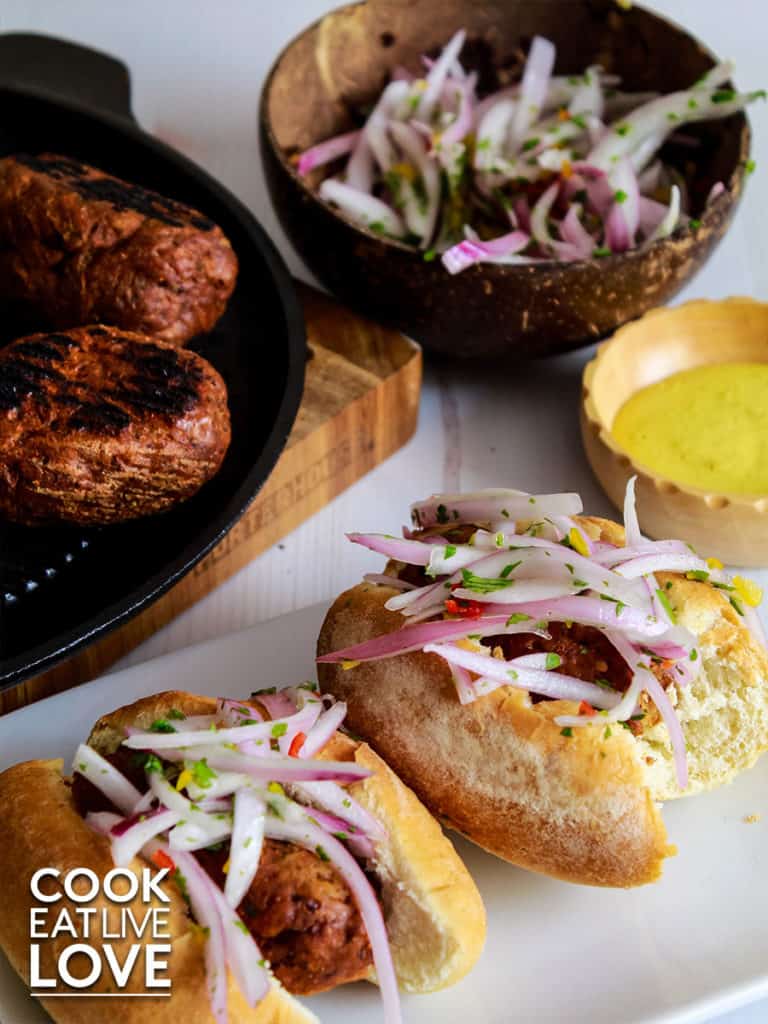 Vegan chorizo in buns topped with sliced onion salad.