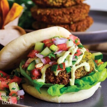 Front view of vegan falafel burger ready to eat with sweet potato fries in back.
