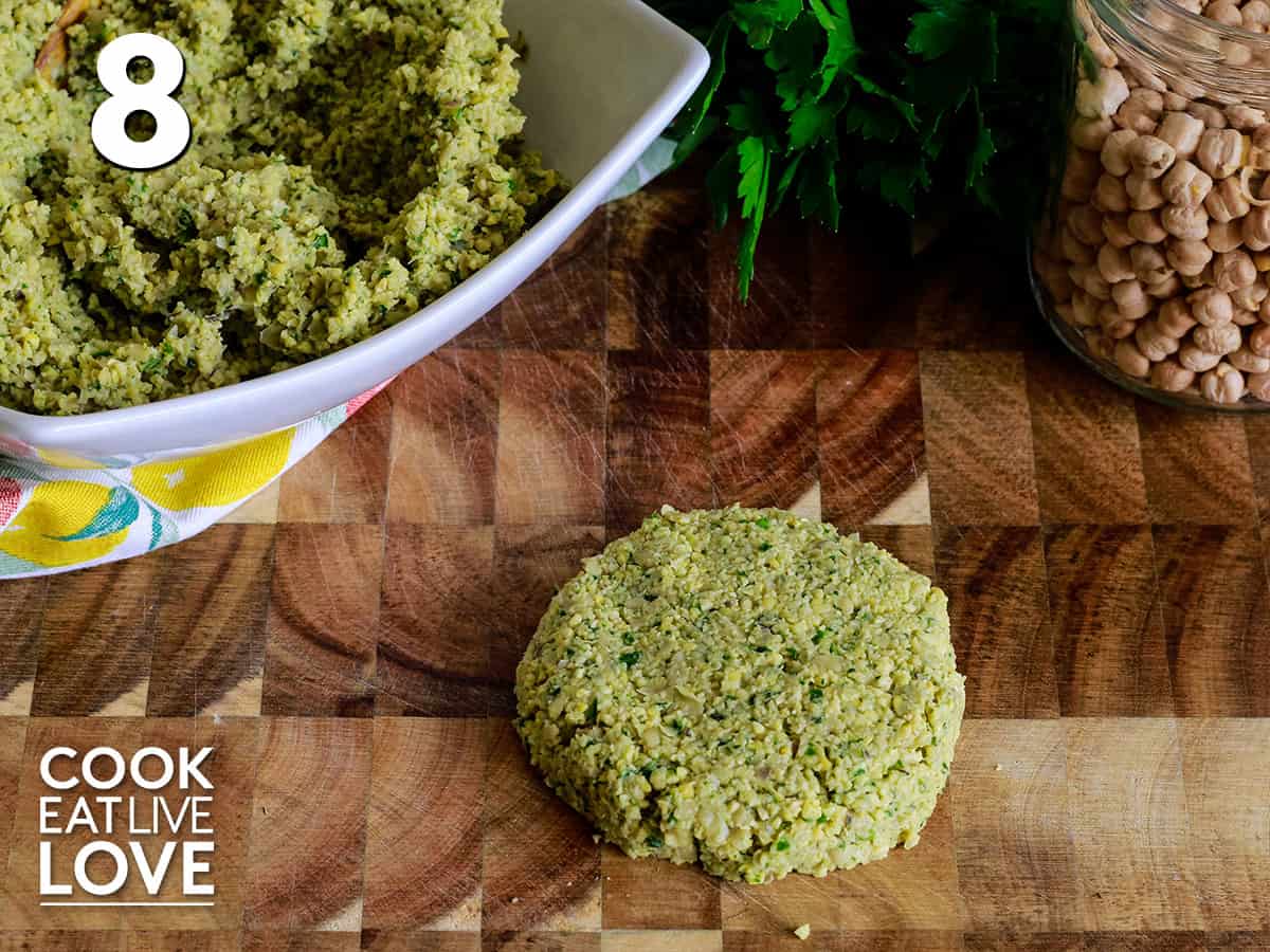 Falafel mixture from half cup measure is shaped into a patty laying on a cutting board.