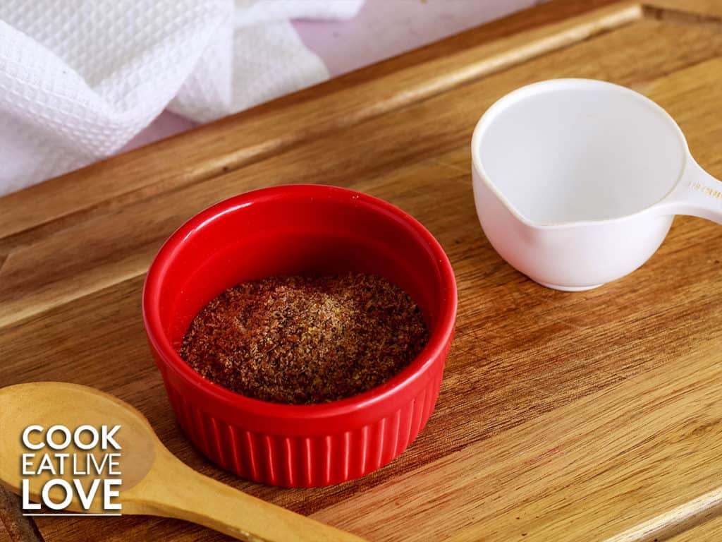 Flax meal in red container with measuring cup of water to the side.