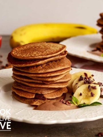 Front view of stack of 10 pancakes on a white plate with sliced bananas, cacao cream and fresh mint.
