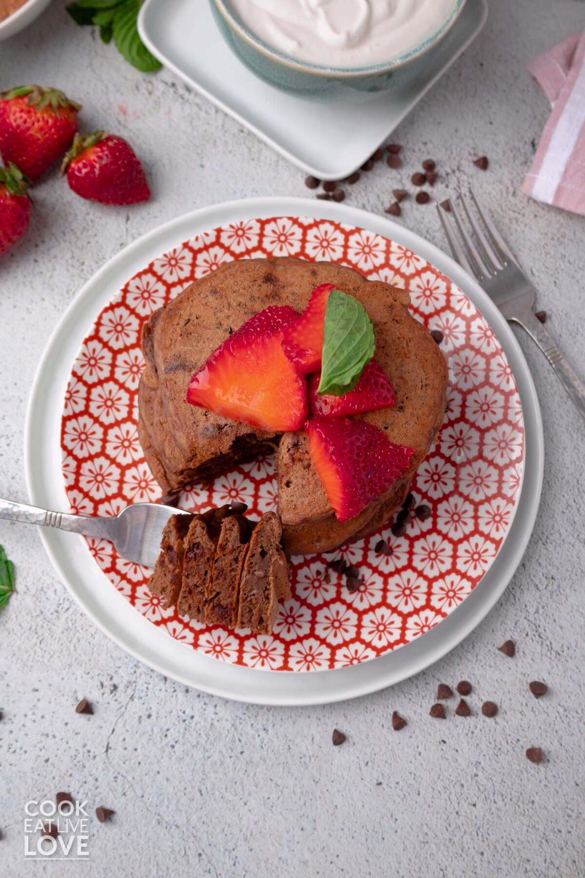 A plate of chocolate protein pancakes with a bite on a fork and laying to the side of the stack.