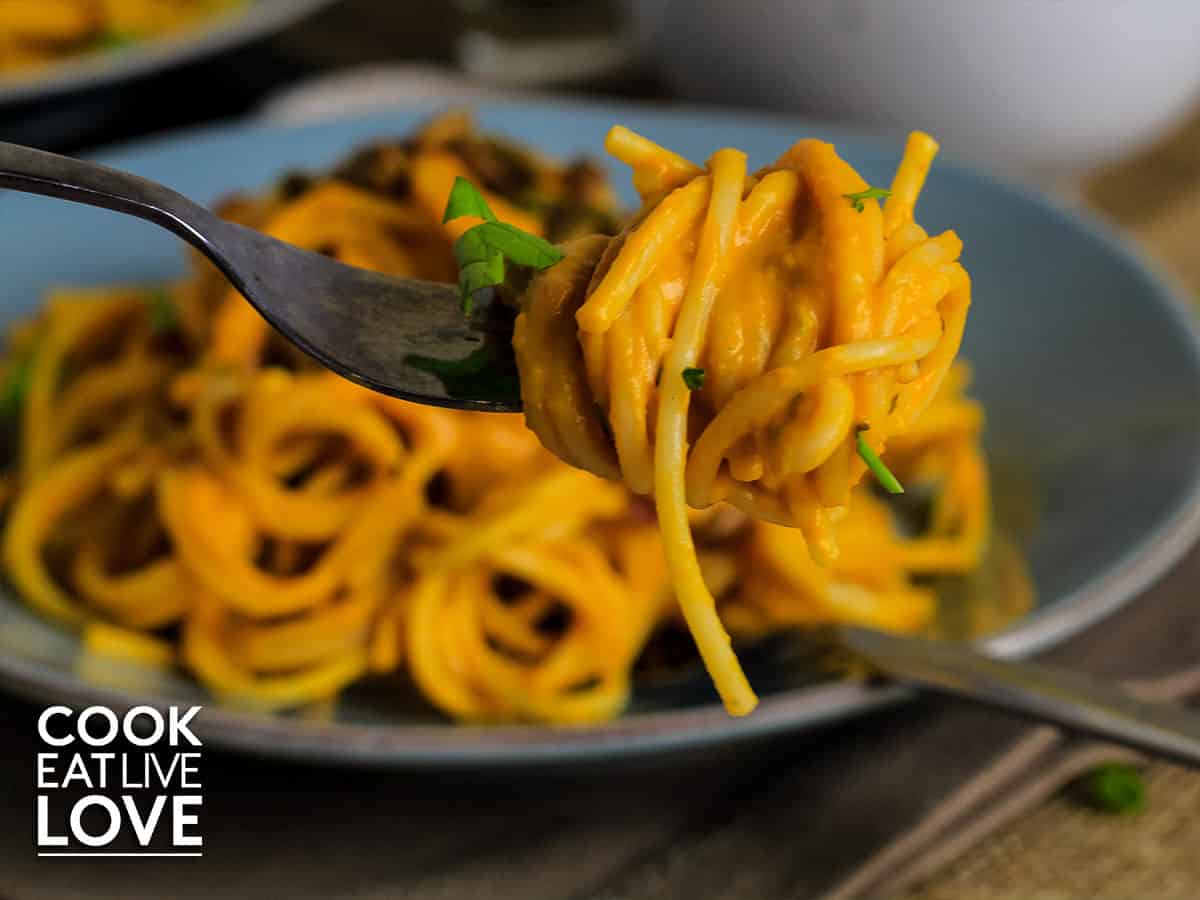 Closeup of vegan butternut squash pasta twirled on a fork with plate of pasta in background.