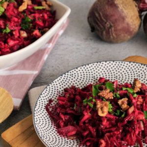 Closeup view of beetroot and apple salad on plate with serving bowl in background.
