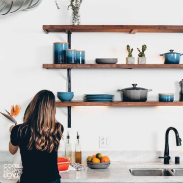 Woman from the back working in her kitchen. With kitchen tools on shelves above her on the wall.