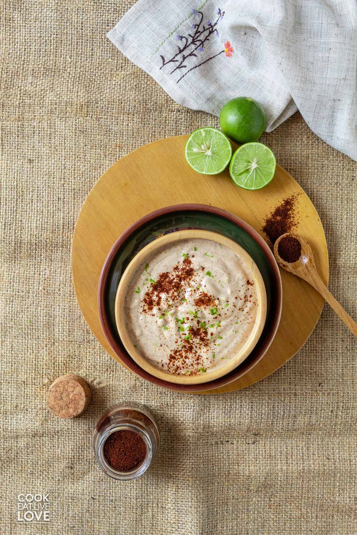 Chipotle yogurt sauce in a bowl on a plate with limes and a spoonful of chipotle chili powder.