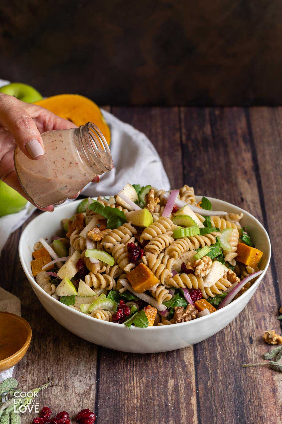 A hand pouring the dressing over the fall pasta salad in a bowl.