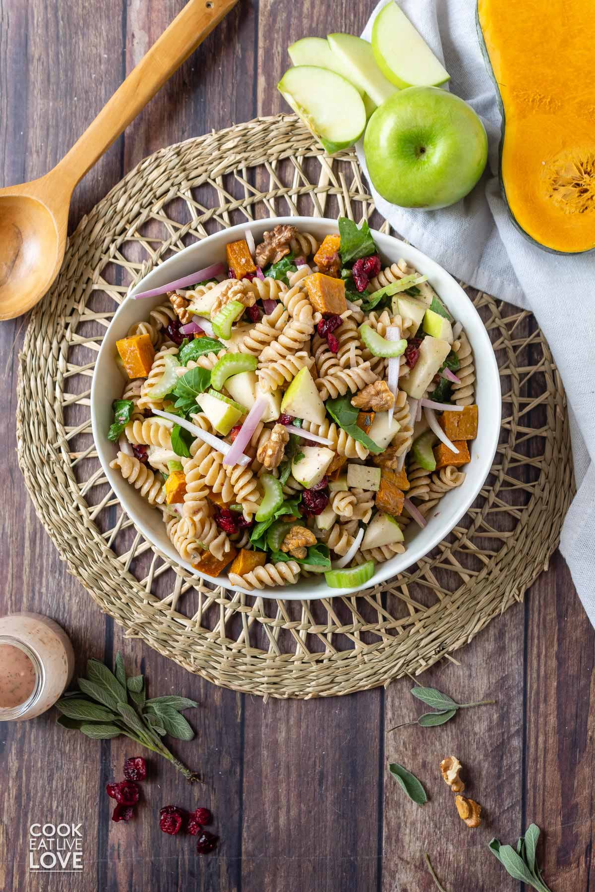 Fall pasta salad on the table with spoon, dressing and apples.