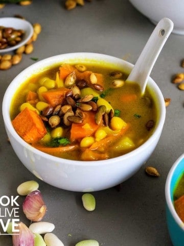 Bowl of healthy pumpkin soup with ceramic white spoon in bowl. Around the bowl are white beans and pumpkin seeds.