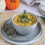 Pumpkin dip in bowl with pumpkin seeds on top served up with pumpkin seeds and herbs.