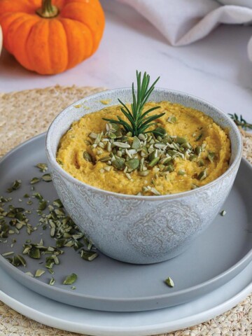 Pumpkin dip in bowl with pumpkin seeds on top served up with pumpkin seeds and herbs.