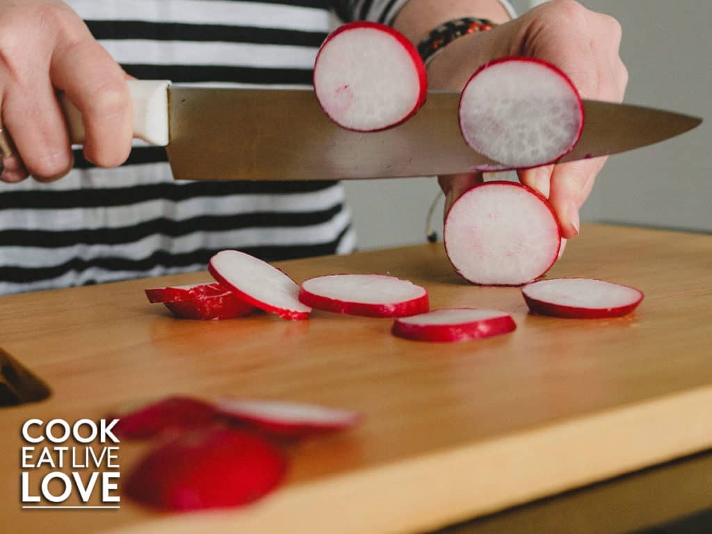 Hand holding knife and cuttting radish on cutting board.
