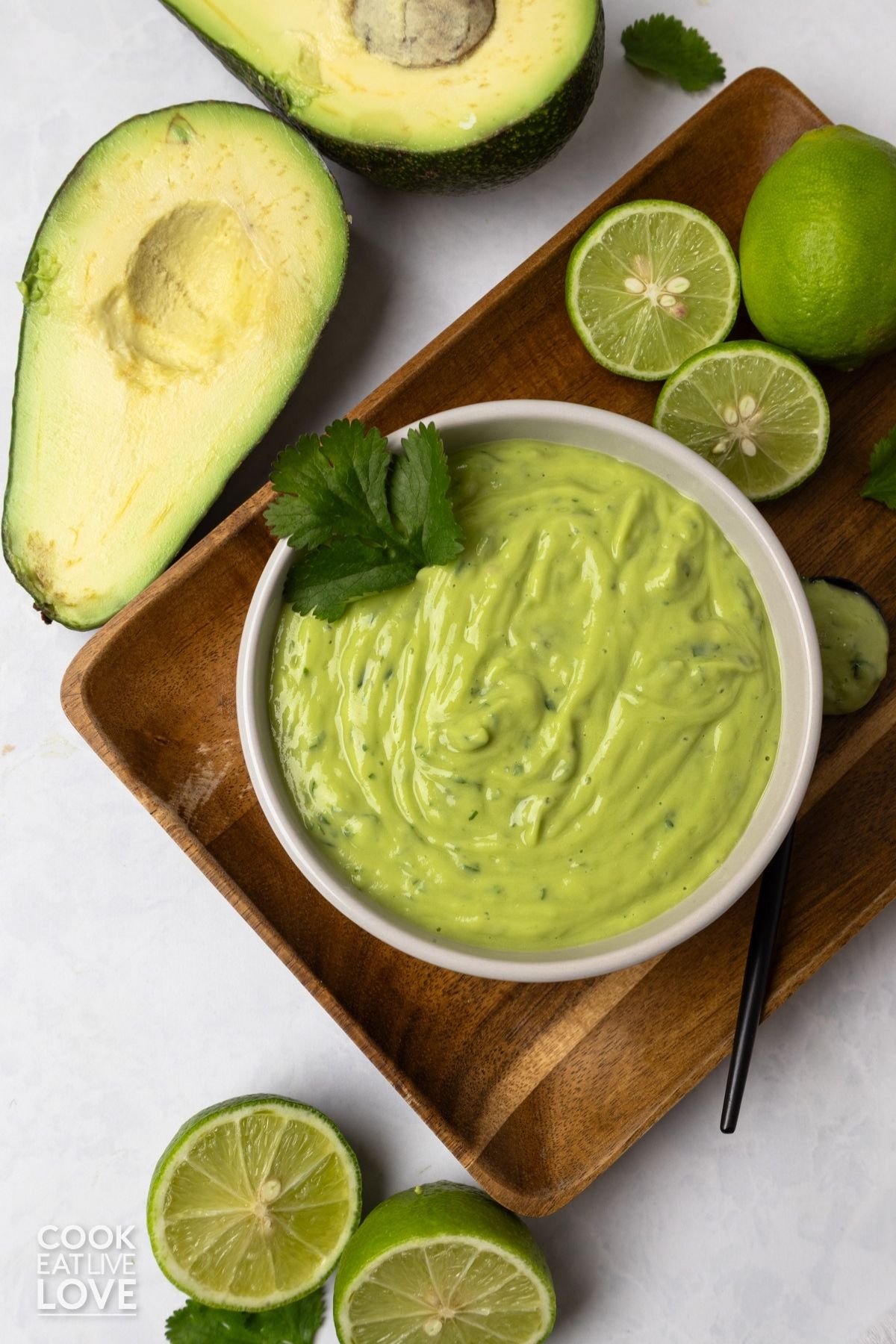 A bowl of avocado sauce with cilantro, limes, and avocado half around the bowl.