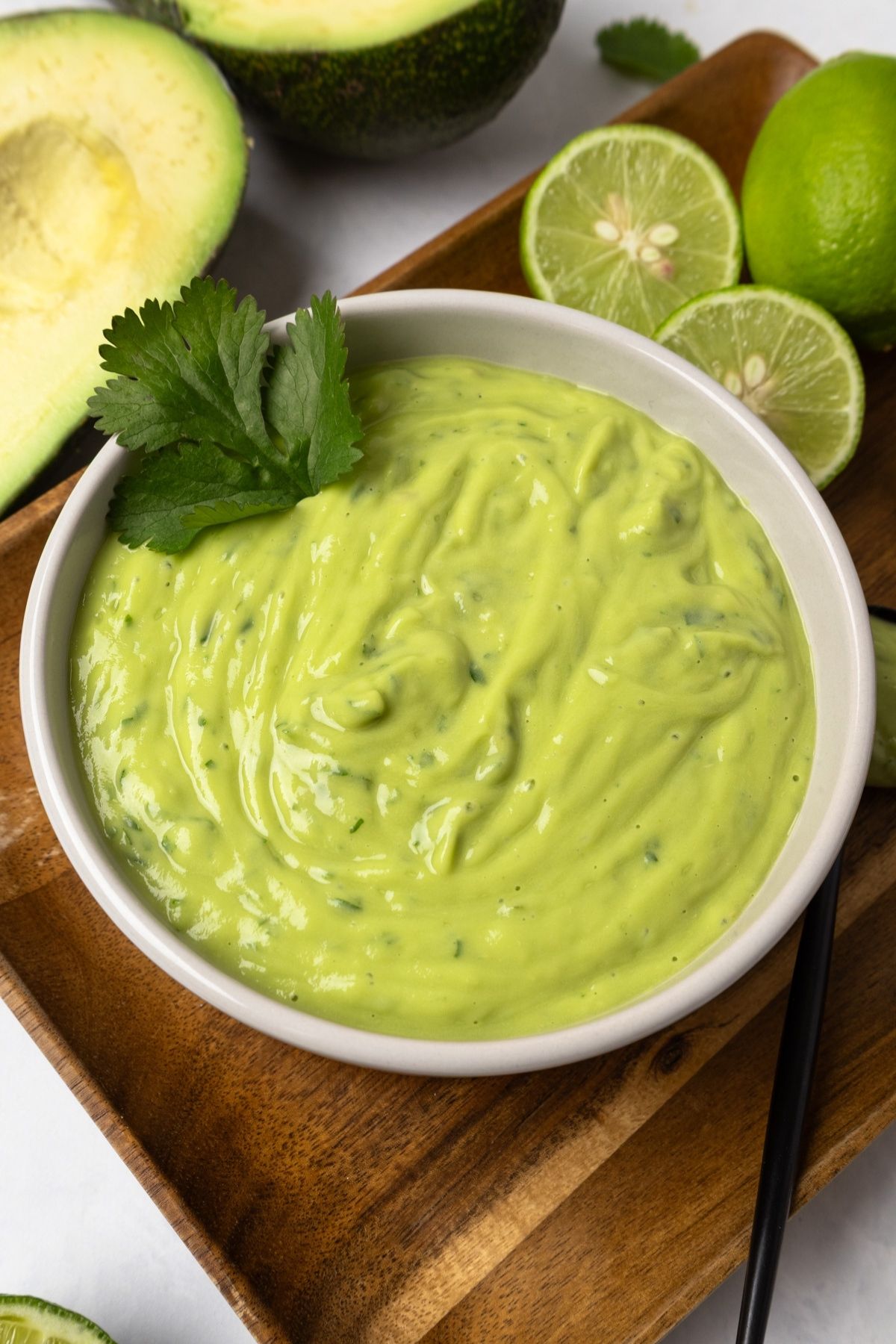A bowl of avocado sauce garnished with cilantro on a wooden board. 